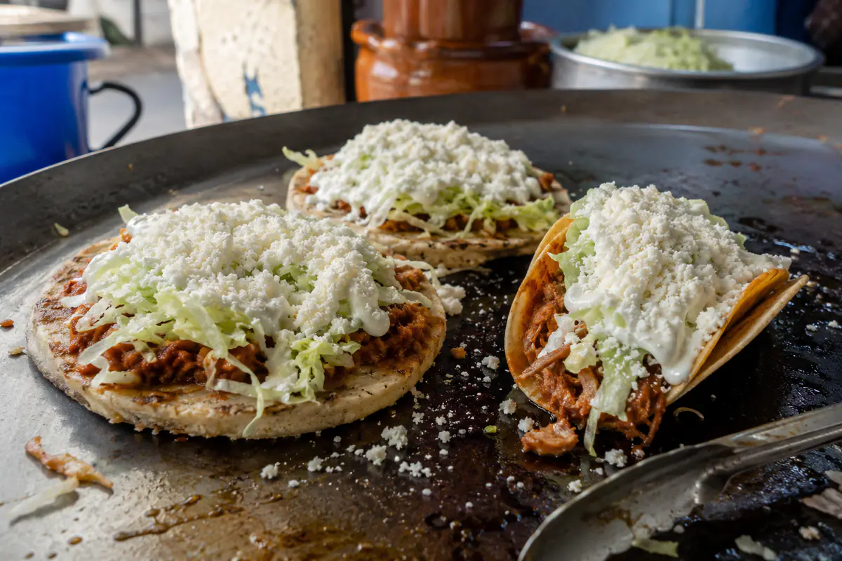 Sopes y tacos rematados con queso cotija análogo espolvoreado en un comal